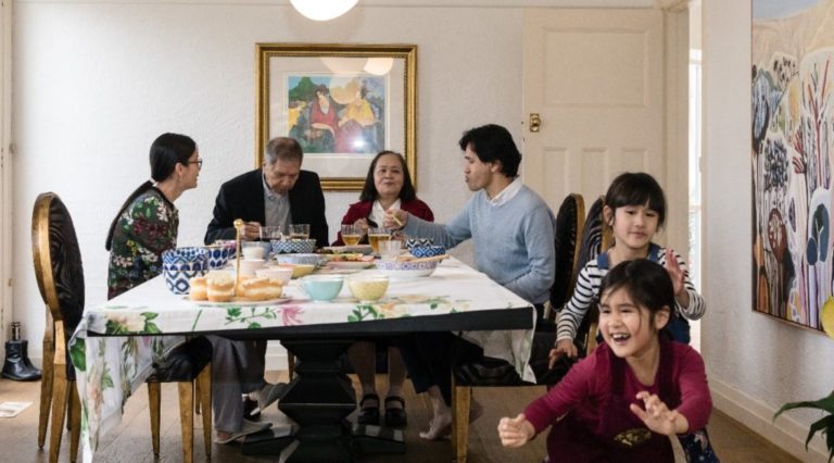 The Phan family seated at their dining table while their children play nearby
