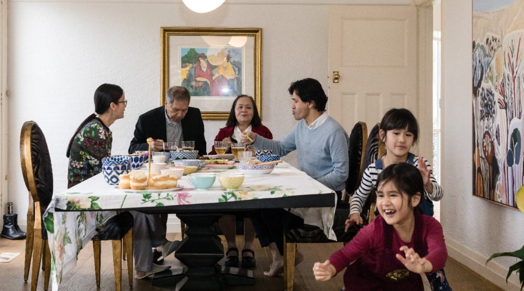 The Phan family seated at their dining table while their children play nearby