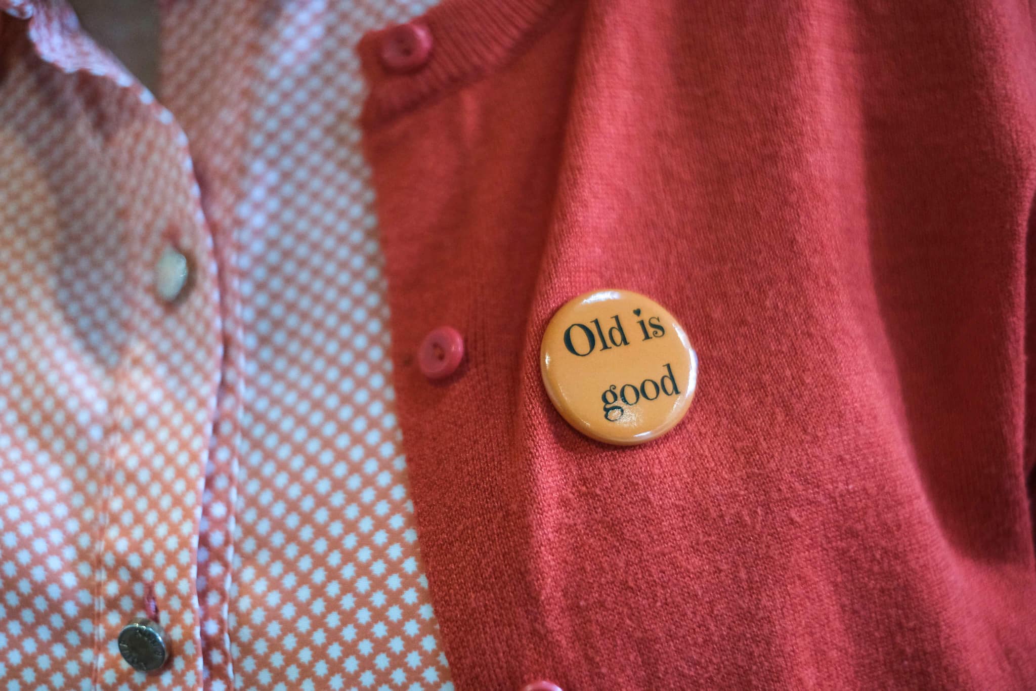 Picture of a button on a pink cardigan with the writing 'Old is good.'